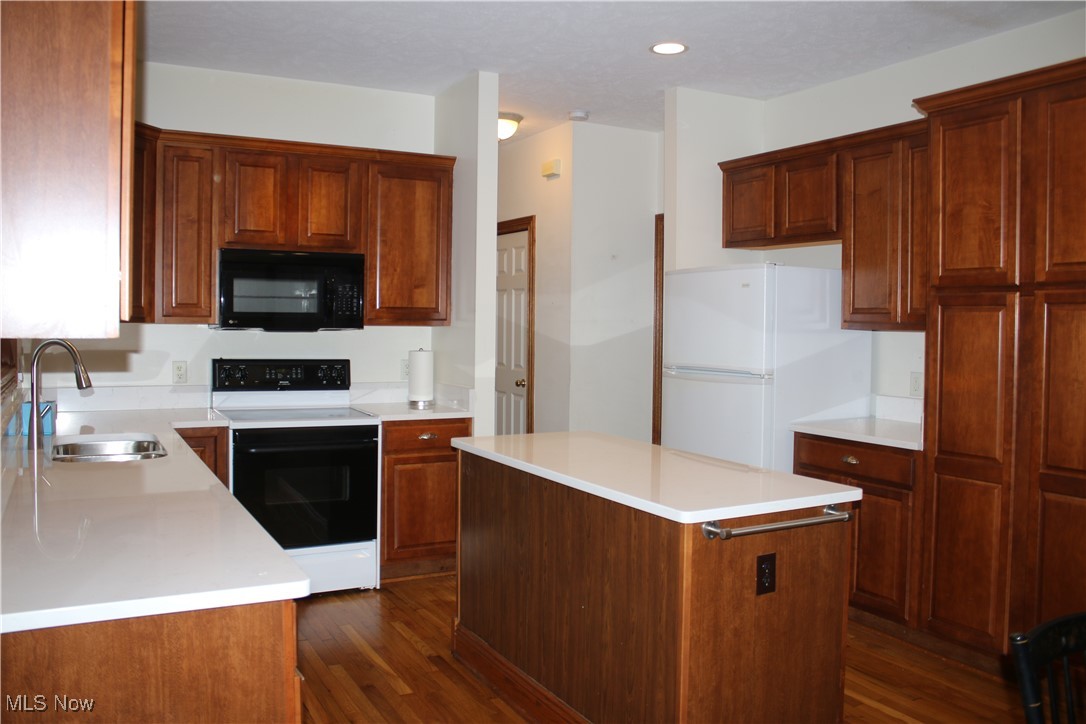 Kitchen featuring range with electric stovetop, freestanding refrigerator, dark wood finished floors, black microwave, and a center island