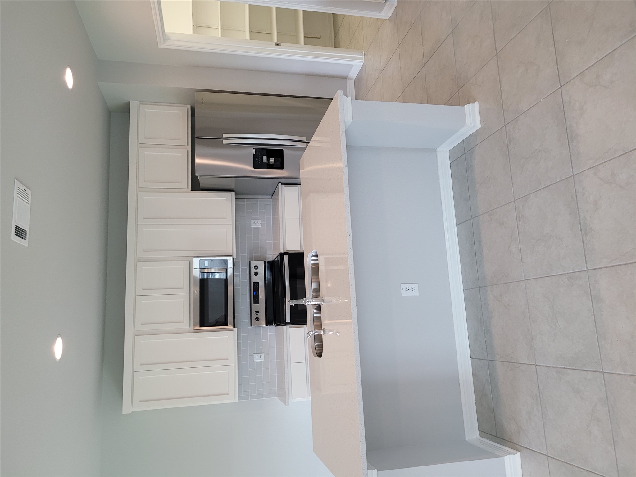 131 Wild Wind Cove Jarrell, TX 76537 - Photo 8 of 26 Kitchen featuring a large central island with a double basin sink, light-toned countertops, white cabinetry, stainless steel appliances, and a tiled backsplash