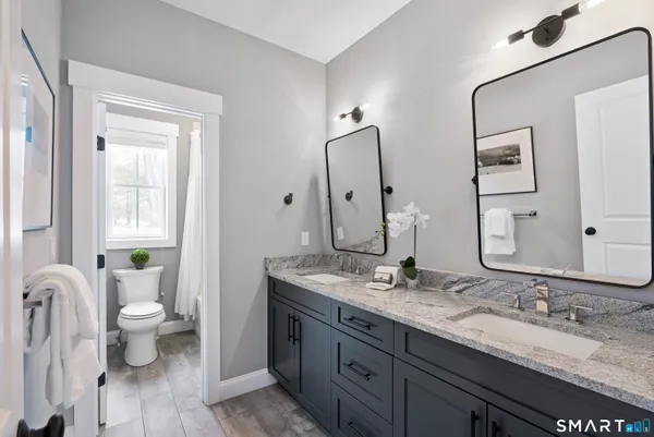 a bathroom with a granite countertop toilet a double vanity sink a mirror and a window