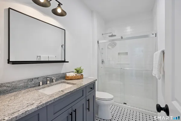 a bathroom with a granite countertop sink a toilet a mirror and shower
