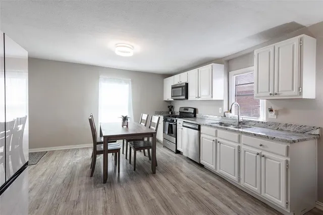 a kitchen with stainless steel appliances granite countertop a dining table chairs a sink and dishwasher a refrigerator with wooden floor