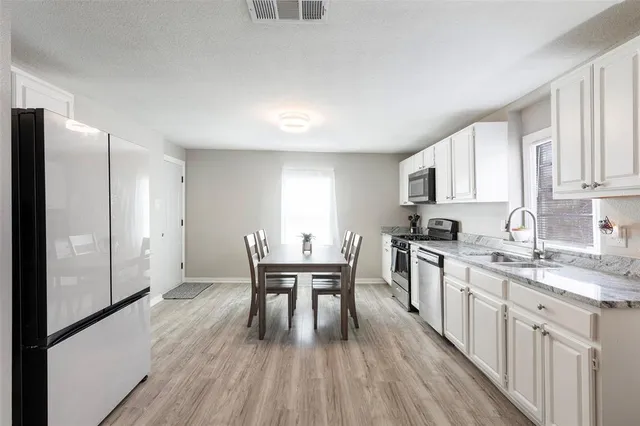 a kitchen with stainless steel appliances granite countertop a refrigerator a stove a sink dishwasher and white cabinets with wooden floor