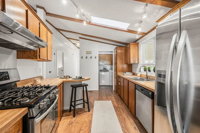 a kitchen with stainless steel appliances granite countertop a stove top oven a sink dishwasher a dining table and chairs with wooden floor