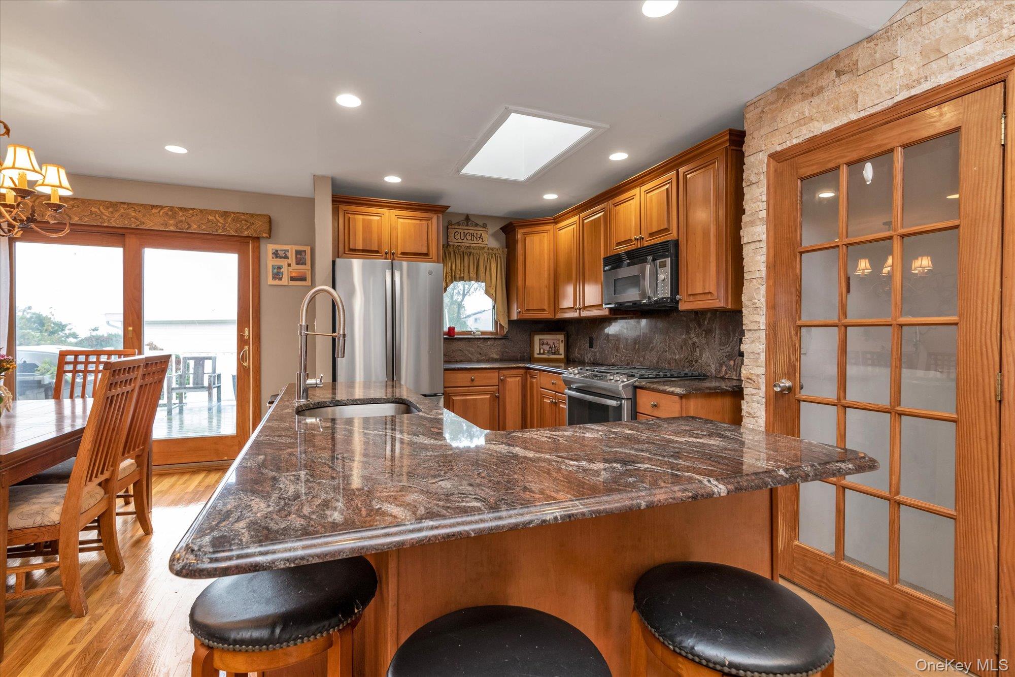 26 Cheshire Road Inwood, NY 11096 - Photo 7 of 22 Kitchen with a kitchen breakfast bar, brown cabinets, appliances with stainless steel finishes, backsplash, and plenty of natural light