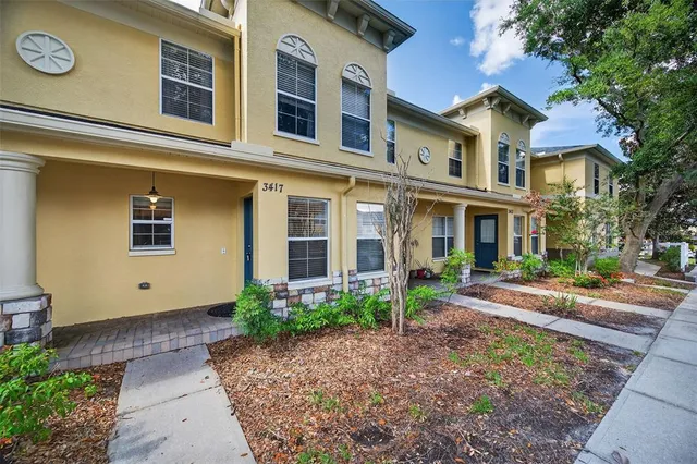 a view of a brick house with many windows plants and large tree