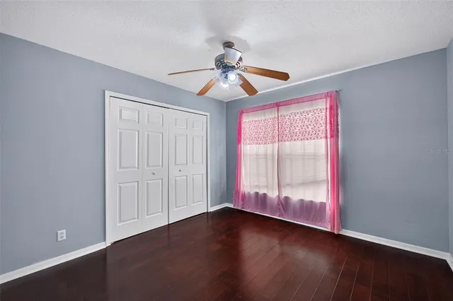 a view of an empty room with wooden floor and a ceiling fan