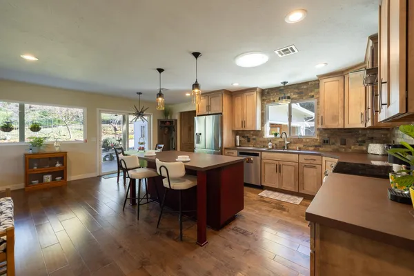 a kitchen with a sink dishwasher a stove a kitchen island with chairs and wooden floor