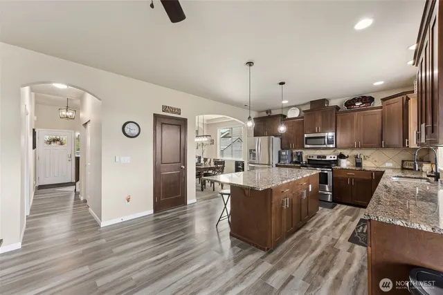 a open kitchen view with stainless steel appliances kitchen island granite countertop a stove a refrigerator a sink a oven and a dining table with wooden floor