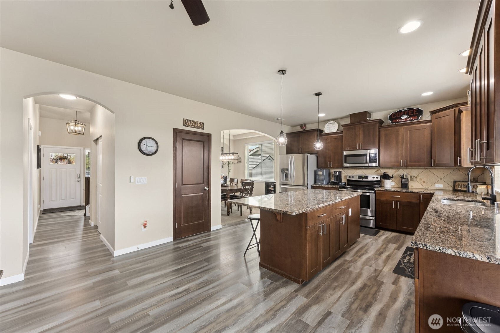 103 Balmer Street Southwest Orting, WA 98360 - Photo 9 of 30 a open kitchen view with stainless steel appliances kitchen island granite countertop a stove a refrigerator a sink a oven and a dining table with wooden floor