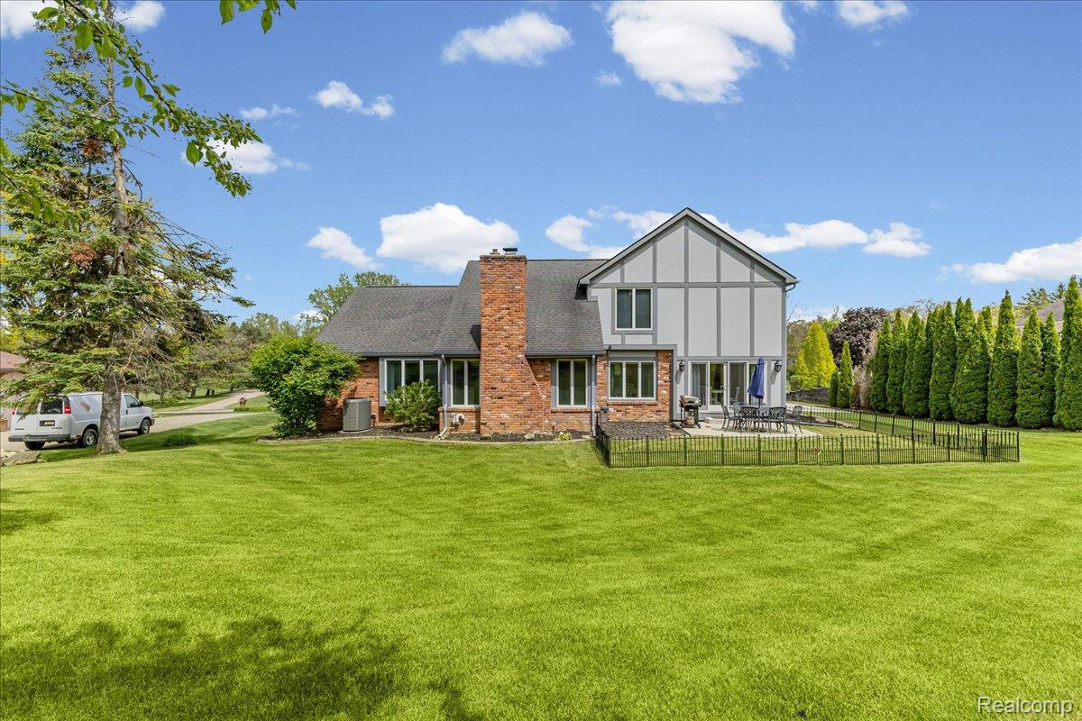 69075 Brookhill Drive Romeo, MI 48065 - Photo 28 of 28 Expansive rear yard featuring a brick and siding exterior, a large patio area, and a black perimeter fence