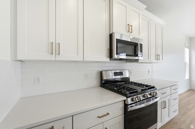 401 West 3085 South, Unit 329 Nibley, UT 84321 - Photo 16 of 34 Kitchen with stainless steel appliances, white cabinets, light wood finished floors, decorative backsplash, and light stone countertops