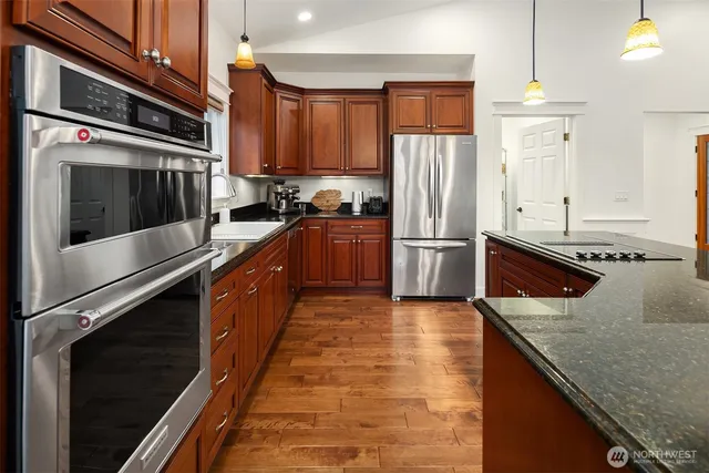 a kitchen with stainless steel appliances granite countertop a refrigerator a stove and a sink with wooden floor