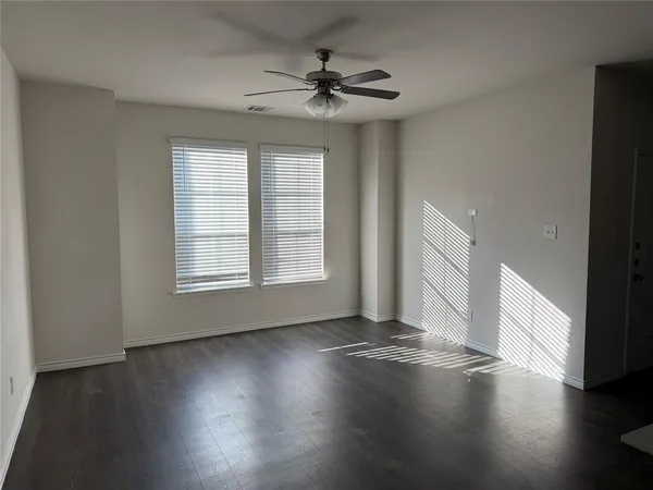 an empty room with wooden floor chandelier fan and windows