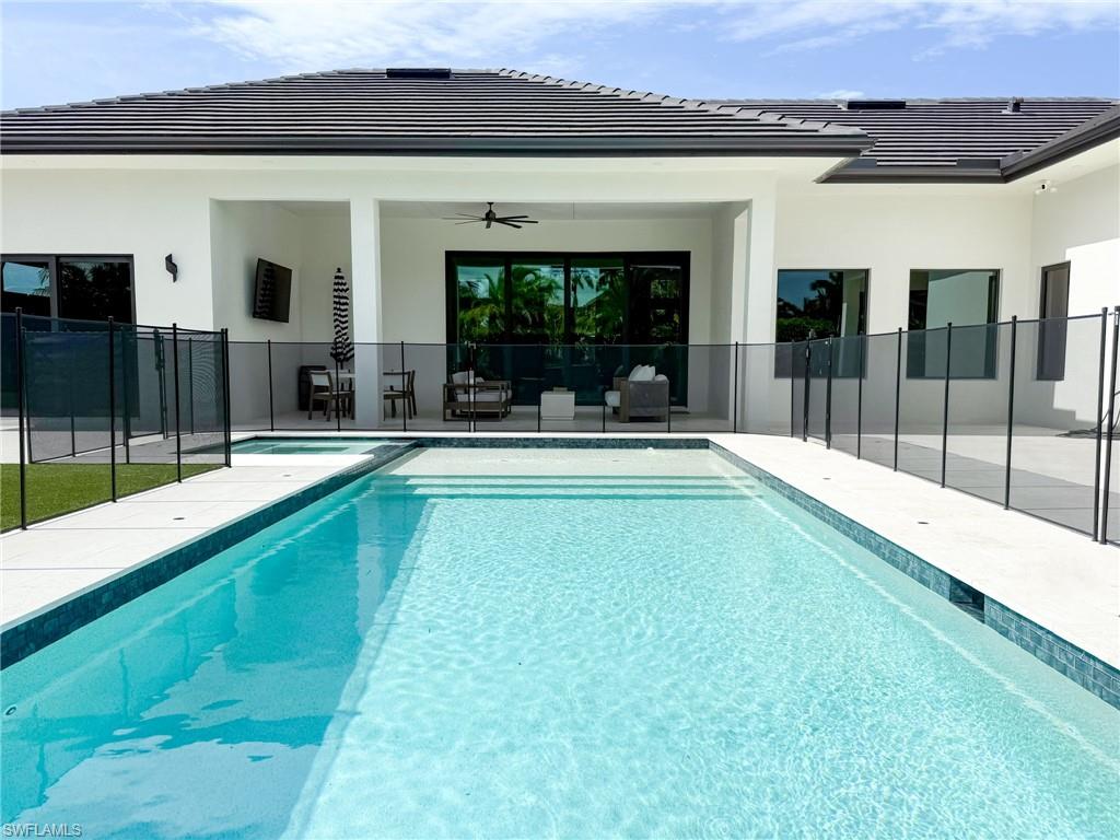 1702 Ludlow Road Marco Island, FL 34145 - Photo 44 of 47 Contemporary home exterior featuring a rectangular pool with integrated spa, expansive white patio decking, a covered lanai with recessed lighting and a ceiling fan, and black-framed windows