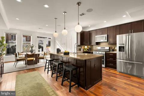 a kitchen with stainless steel appliances granite countertop a refrigerator a stove a sink a dining table and chairs with wooden floor