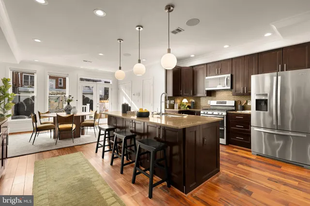 a kitchen with stainless steel appliances granite countertop a refrigerator a stove a sink a dining table and chairs with wooden floor