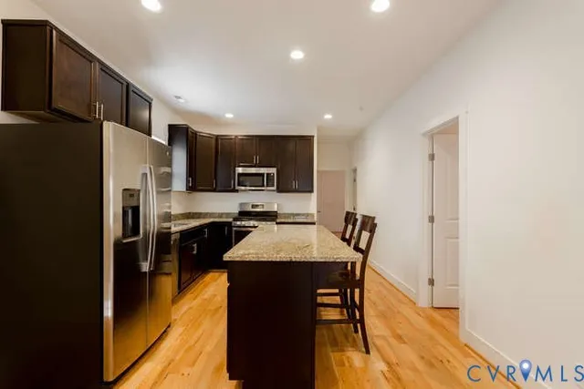 a kitchen with stainless steel appliances granite countertop a refrigerator a stove top oven a sink dishwasher and wooden cabinets with wooden floor