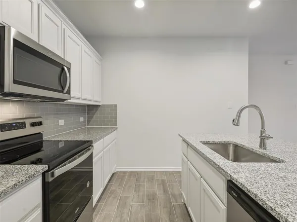 a kitchen with granite countertop a sink dishwasher stove and microwave with wooden floor