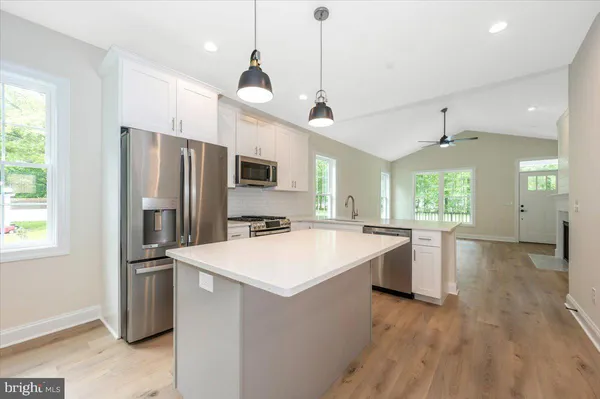 a open kitchen with stainless steel appliances granite countertop a refrigerator a sink dishwasher a stove and white countertops with wooden floor