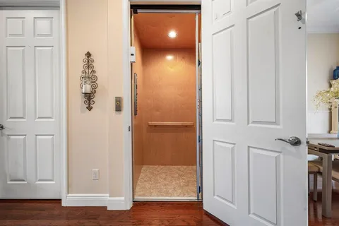 a view of a elevator and an empty room with wooden floor