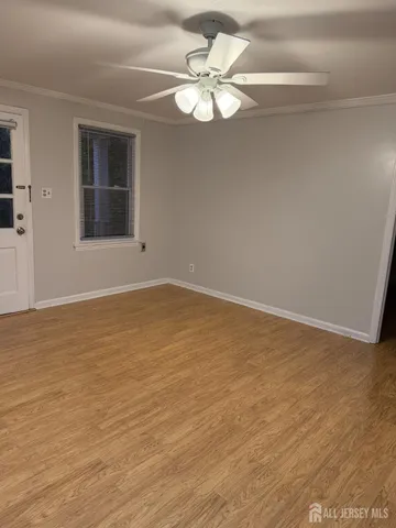 a view of an empty room with wooden floor and a ceiling fan