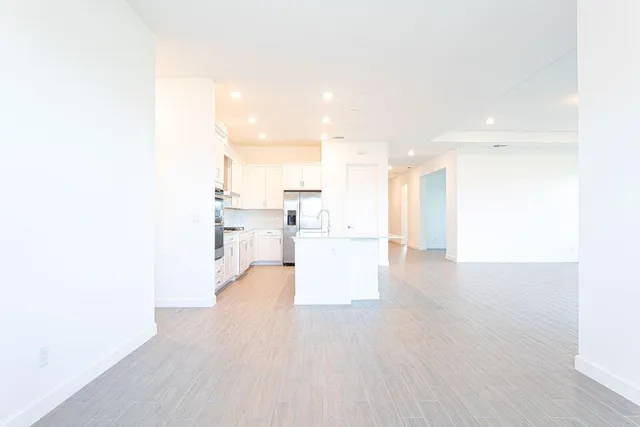 a large kitchen with stainless steel appliances a large counter top a stove a refrigerator and white cabinets