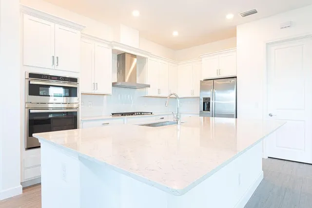 a kitchen with stainless steel appliances granite countertop a sink and white cabinets with wooden floor