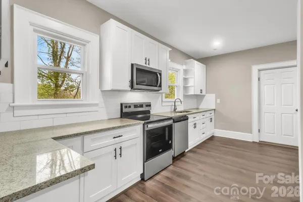 a kitchen with stainless steel appliances granite countertop a stove top oven a sink dishwasher and white cabinets with wooden floor