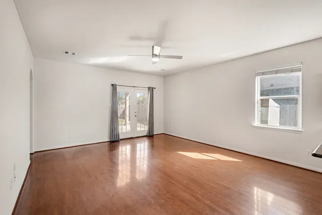 an empty room with wooden floor chandelier fan and windows