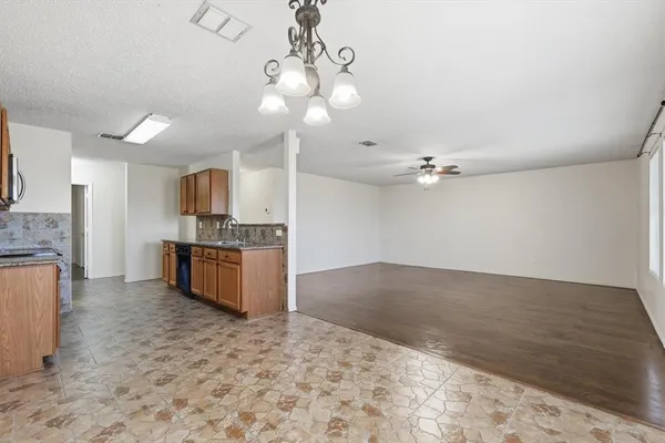 a kitchen with granite countertop stainless steel appliances a sink dishwasher a stove top oven a refrigerator with wooden cabinets and floor