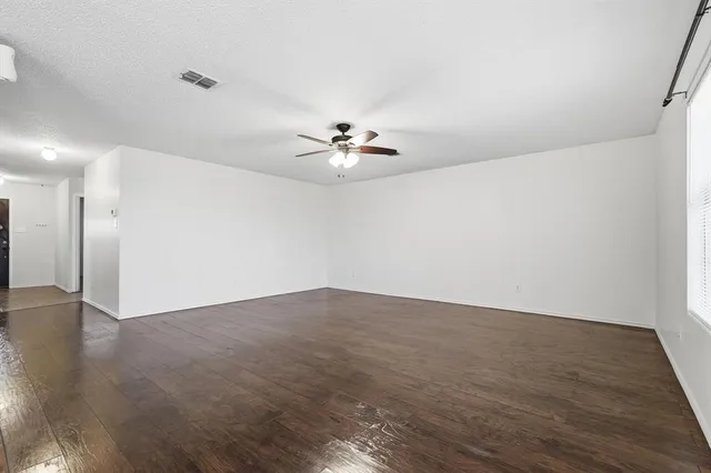 an empty room with wooden floor chandelier fan and windows