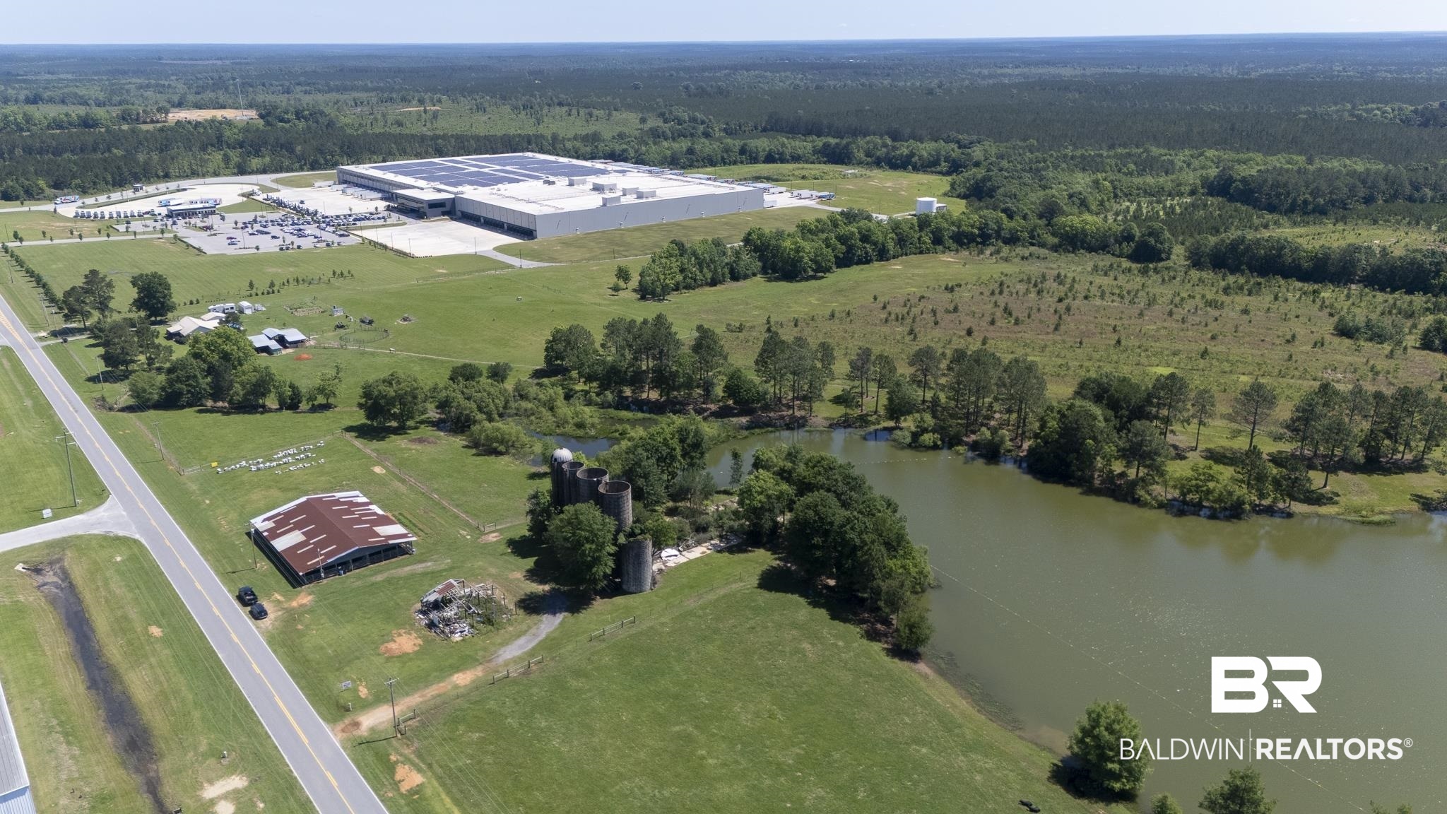 30580 County Road 49 Loxley, AL 36551 - Photo 13 of 32 Expansive green landscape featuring a large industrial building with a solar panel array, a serene body of water, and forested areas