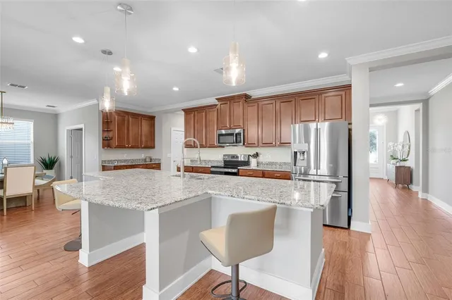 a large kitchen with stainless steel appliances granite countertop a stove a sink a refrigerator and a dining table with wooden floor