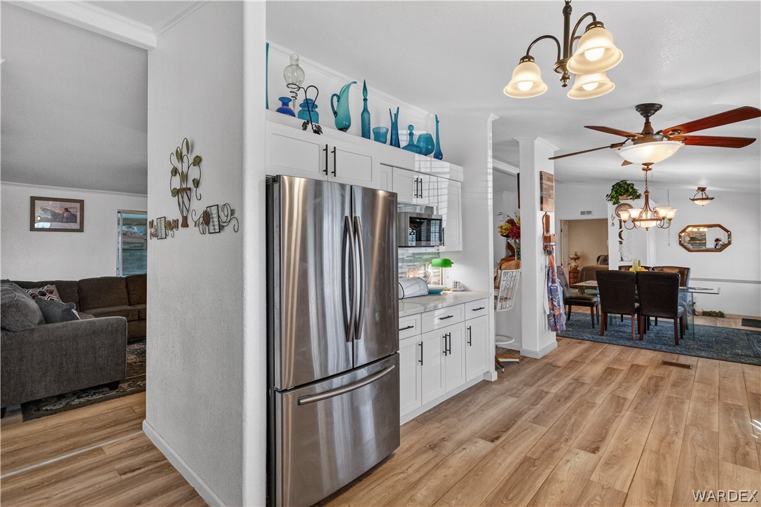 784 Pegasus Ranch Road Bullhead City, AZ 86429 - Photo 17 of 100 Kitchen and dining areas featuring wood-finish flooring, white cabinetry with dark hardware, stainless steel refrigerator, and built-in microwave