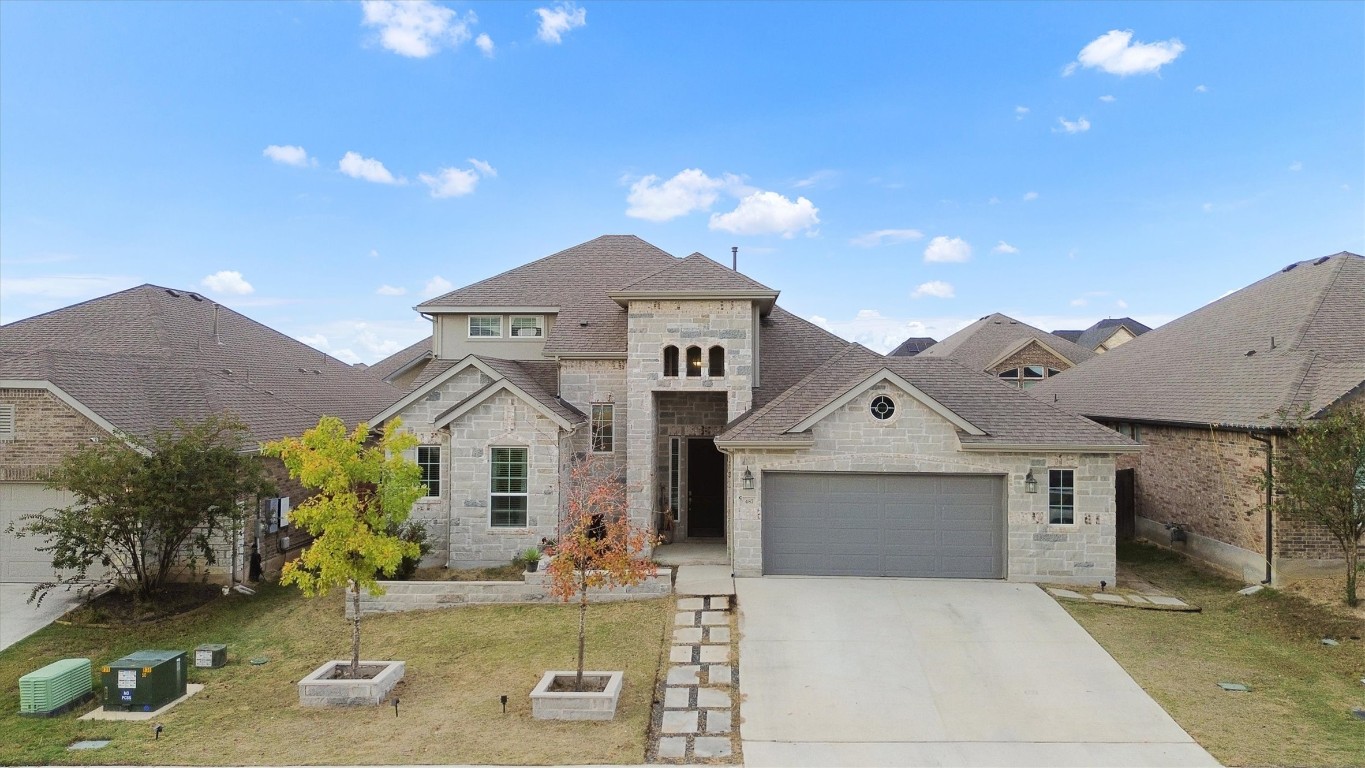 French country inspired facade with stone siding, driveway, an attached garage, a front yard, and a shingled roof