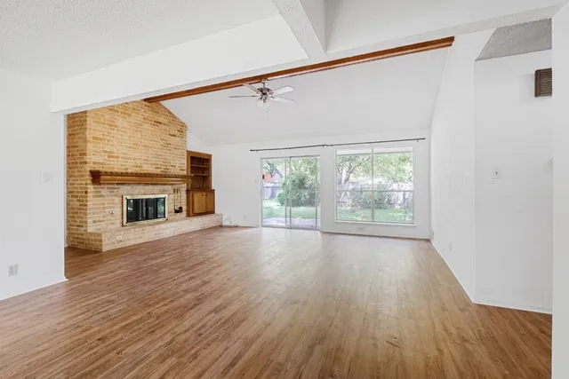 an empty room with wooden floor fireplace and windows