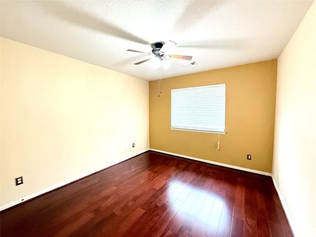 an empty room with wooden floor fan and windows