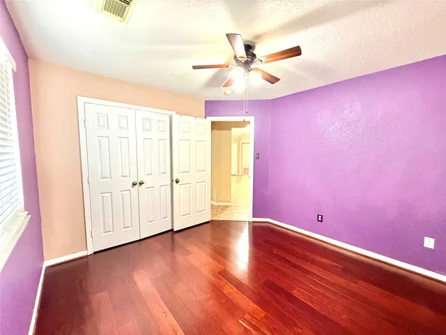 an empty room with wooden floor fan and windows
