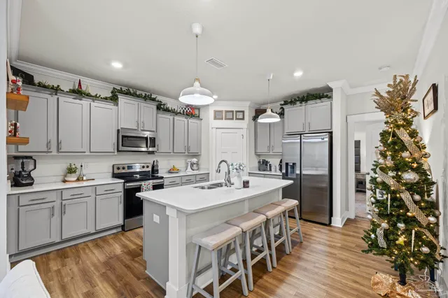 a kitchen with stainless steel appliances a sink a stove a refrigerator cabinets and a dining table with wooden floor