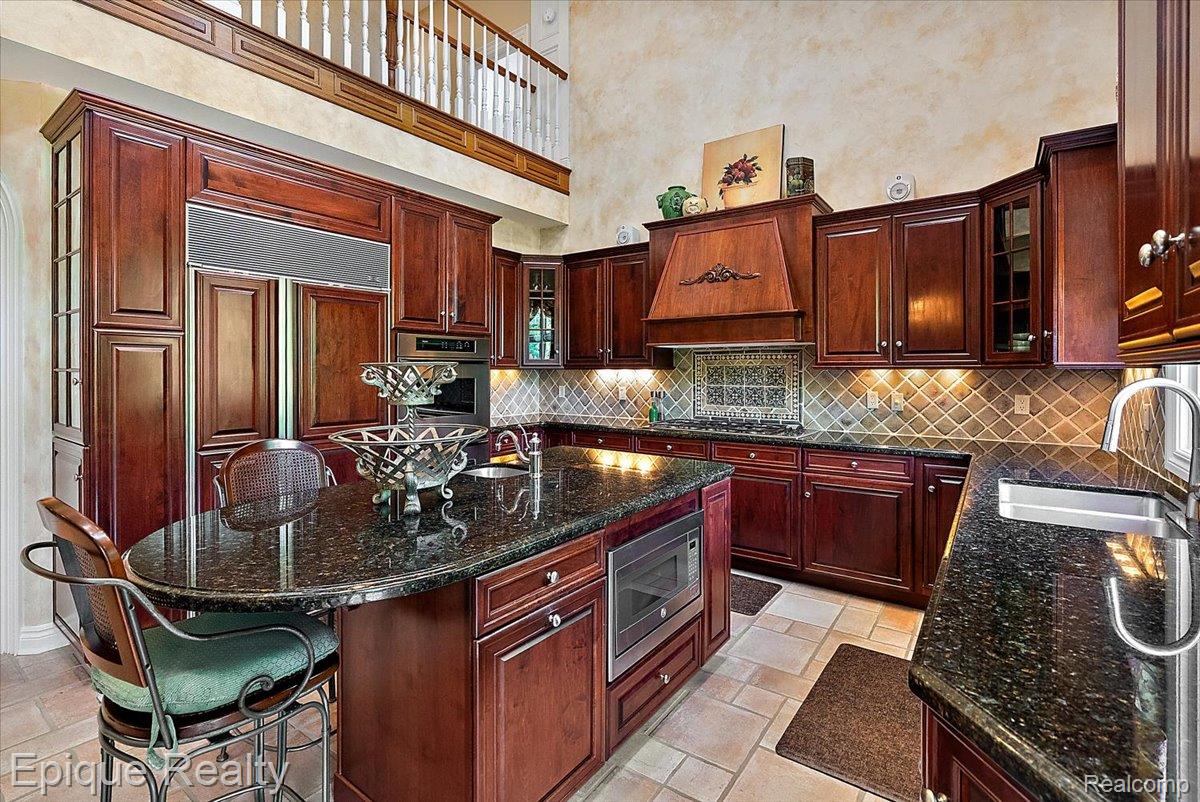 7662 Devins Ridge Clarkston, MI 48348 - Photo 32 of 81 Gourmet kitchen featuring rich wood cabinetry, dark granite countertops, stainless steel appliances, a tiled backsplash, and an expansive kitchen island with bar seating