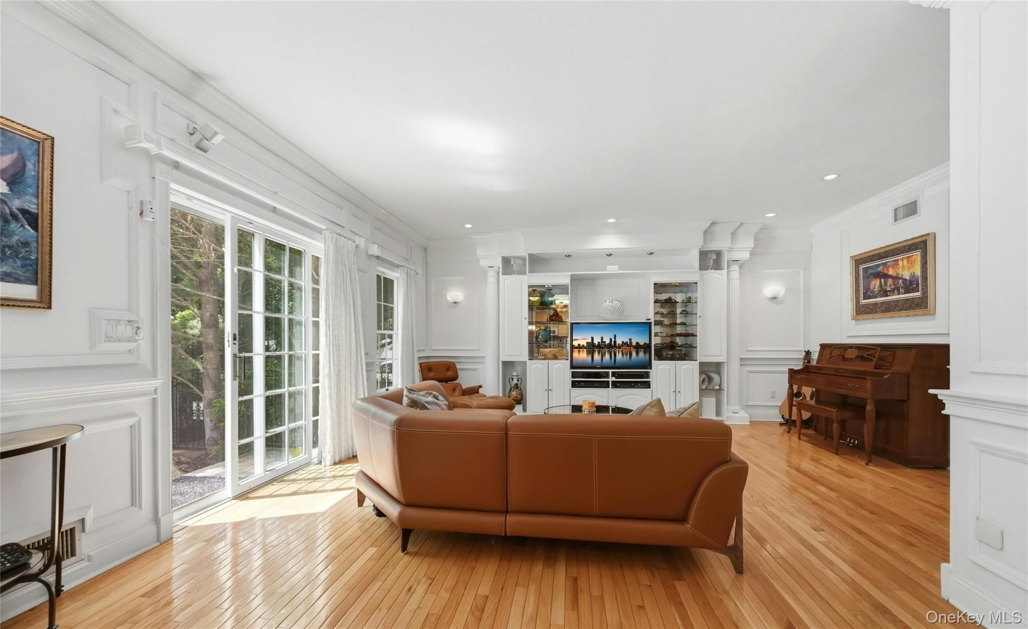 6 Thunder Road Miller Place, NY 11764 - Photo 20 of 50 The Expansive 20'3" x 18'8" Den/Family Room Was Expanded Two Feet Out The Back Of The Home & An Additional Two Feet Towards The Garage Offering A Perfect, Vast Space For Entertaining With 9' Ceilings, Stunning Box Paneled/Wainscoted Walls, Beautiful Hardwood Floors, Andersen Sliding Doors & Oversized Windows Overlooking The Backyard & In Ground Pool, A Striking Custom Built Wall Unit/Entertainment Center With Magnificent Crown Moldings, Columns, Glass Doors & Shelving, Built In Television (Which Stays With The Home) & Built In Lighting, Ample Room For A Very Large Furniture/Seating Area, And Access To The Half Bathroom/Powder Room & Two Car Garage.