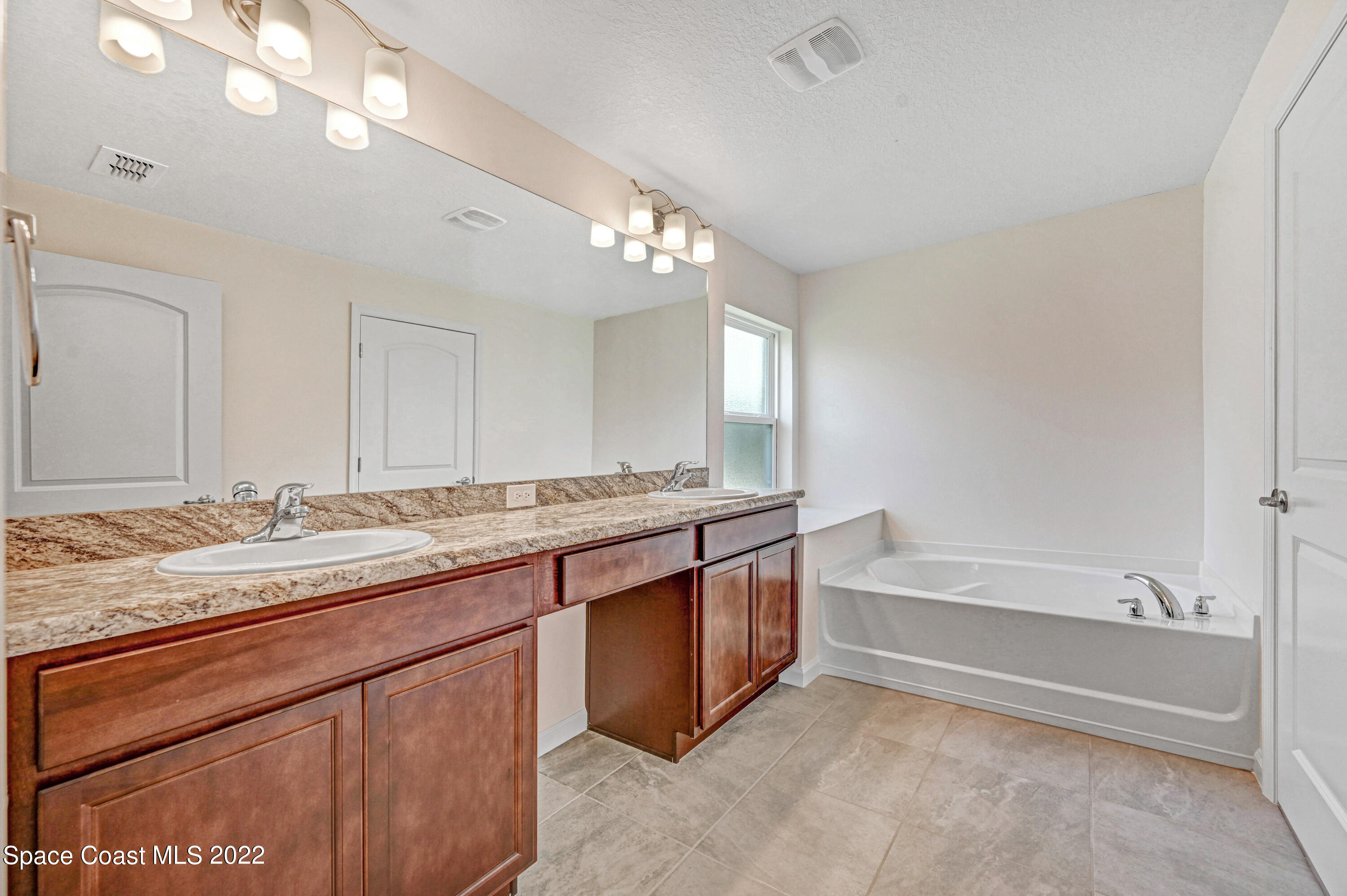 561 Scenic Road Palm Bay, FL 32908 - Photo 35 of 40 a bathroom with a granite countertop bathtub a double vanity sink and a mirror