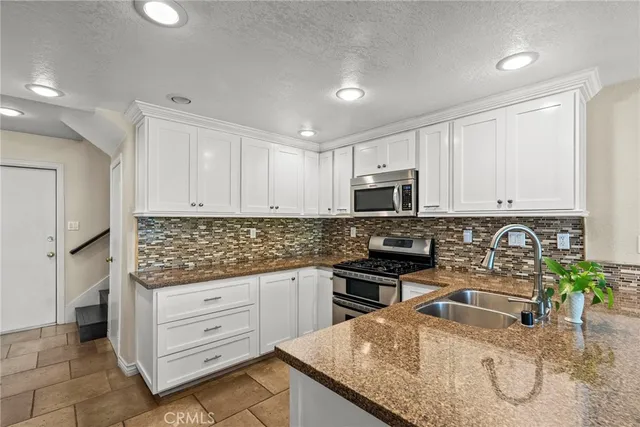 a kitchen with granite countertop a sink a stove top oven and cabinets