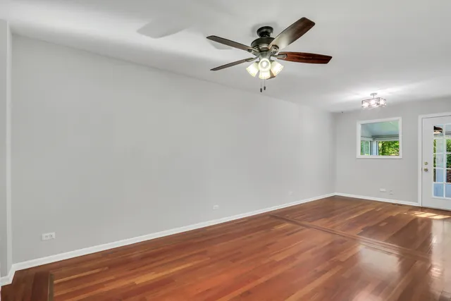 an empty room with wooden floor chandelier fan and windows