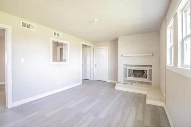 an empty room with wooden floor a fireplace and windows