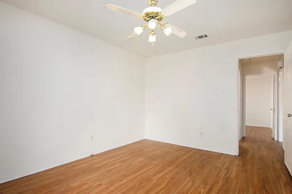 an empty room with wooden floor and a ceiling fan