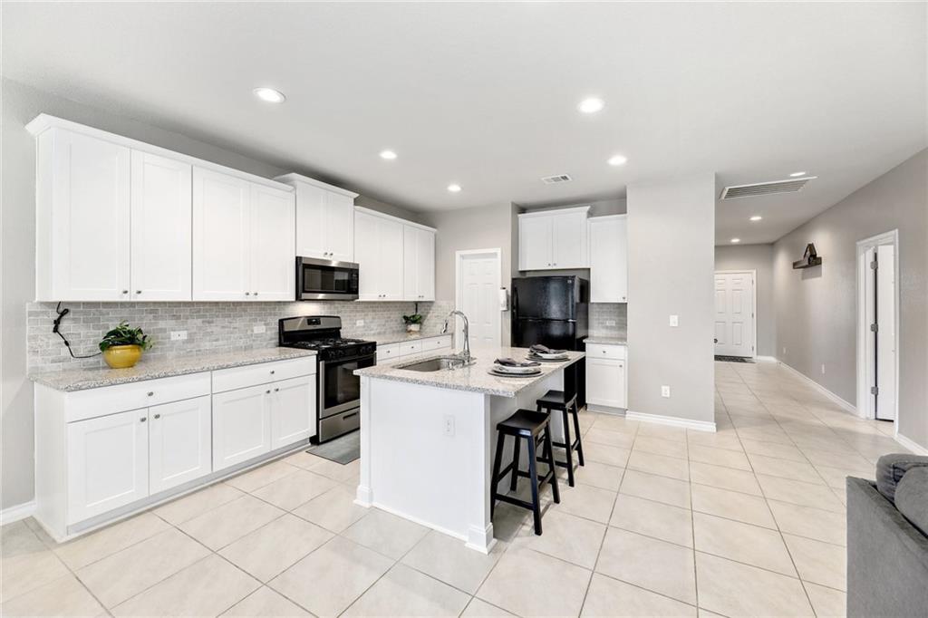 204 Tulum Terrace Leander, TX 78641 - Photo 3 of 22 Kitchen featuring a breakfast bar area, stainless steel appliances, white cabinetry, a kitchen island with sink, and light tile patterned floors