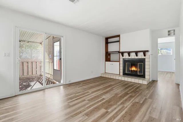 a view of an empty room with wooden floor fireplace and a window