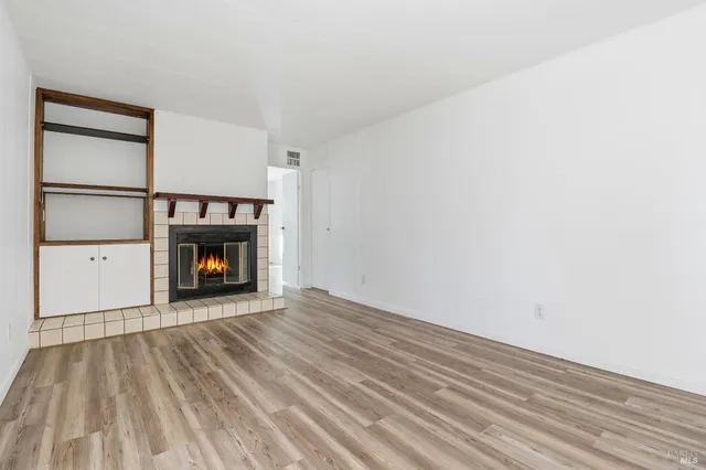 a view of an empty room with wooden floor fireplace and a window