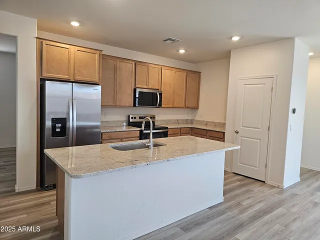 a kitchen with stainless steel appliances granite countertop a refrigerator a sink a stove a microwave and island with wooden floor